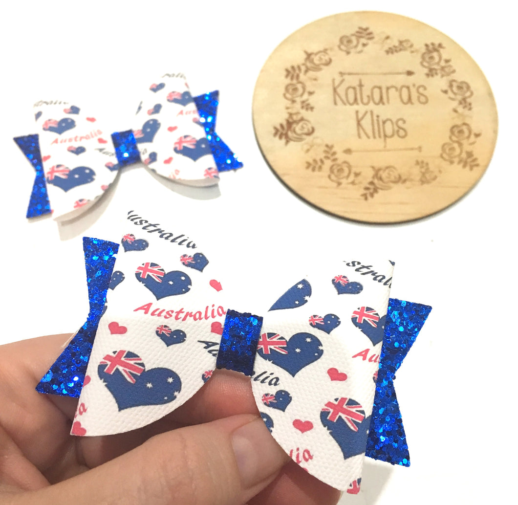 Glitter bow handmade in Australia using quality materials. Heart shaped Australian flag and Australia text on white fabric on top of blue glitter bow.
