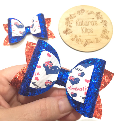 Handmade hair bow in Australia Day theme. Heart shaped Australian Flag and Australia Day text print on blue glitter bow as middle layer. Red glitter bow on bottom layer
